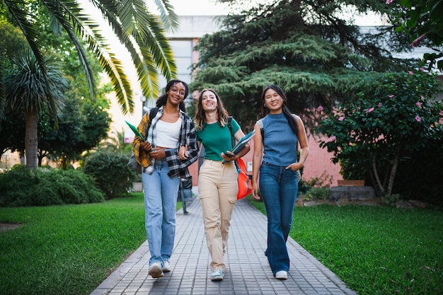 A diverse group of college students smiling and walking on campus. The scene shows a sunny day with green trees and college buildings in the background.