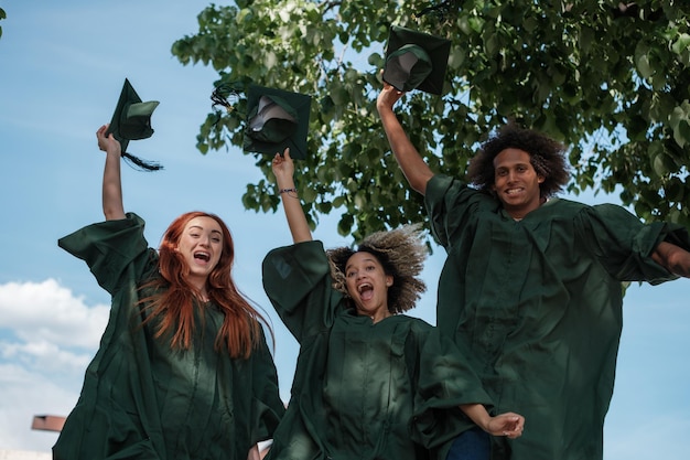 Students celebrating at a college graduation ceremony. They are throwing their hats in the air, and smiles are plastered on their faces. The backdrop is a picturesque campus with lush greenery.