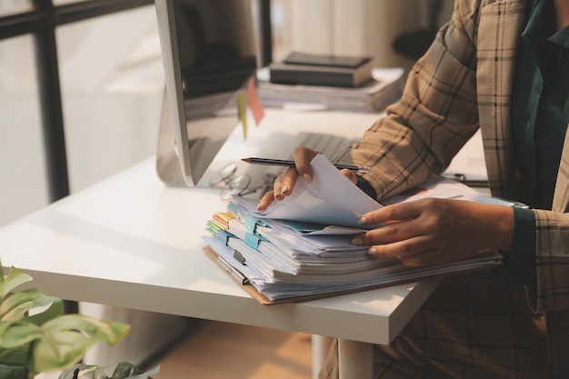 A close-up of a person's hands organizing documents on a desk. The documents include tax forms, pay stubs, and utility bills. The hands are neatly arranging the papers in a folder.