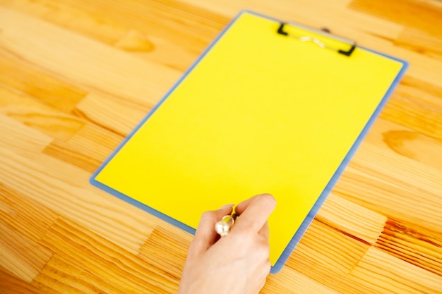 A close-up shot of someone's hand highlighting key words in a college application essay prompt with a bright yellow highlighter. The prompt is printed on a clean white page.