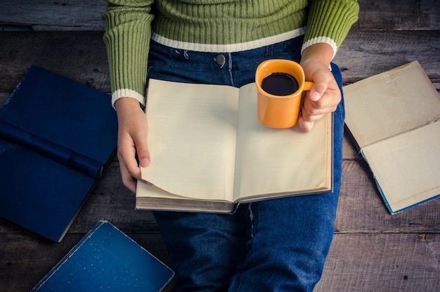 A person holding an open book with brightly colored sticky notes marking various pages. The book is resting on a wooden table next to a cup of coffee and a pair of glasses.