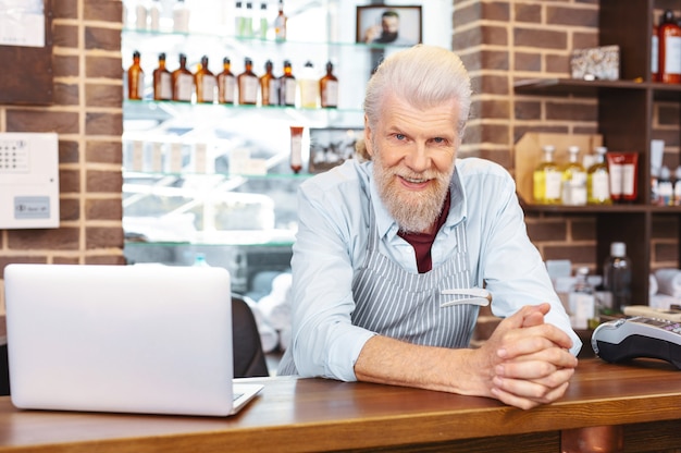 A senior man smiling while talking to a pharmacist about a prescription discount program, with prescription bottles on the counter in the background.