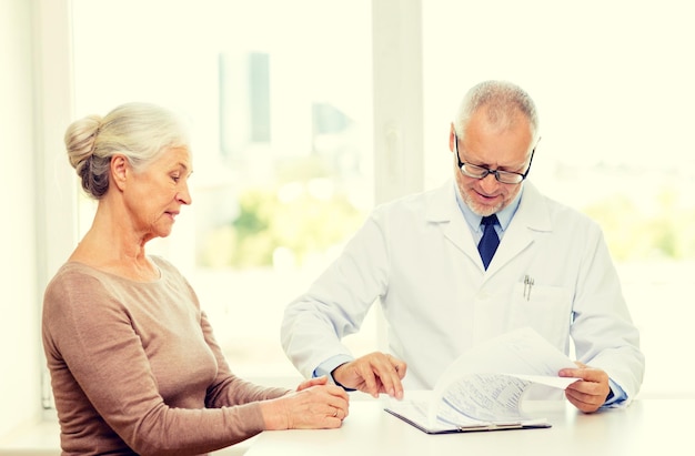 A smiling doctor hands a prescription to a senior patient in an exam room.