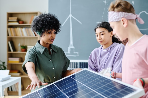 A group of students working on a sustainable energy project in a lab, inspecting solar panels and discussing technical specifications. The setting is a modern, well-equipped laboratory.